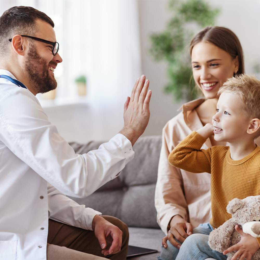a doctor and a child high fiving and the mom smiles